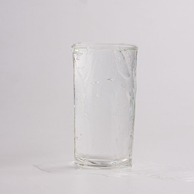 Stock photo of a glass of water that has overflowed and a small puddle of water beside it
