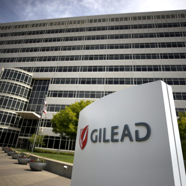 A Gilead Sciences sign stands in front of its headquarters under a blue sky with vignette — first opinion coverage from STAT